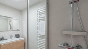 Une salle de bain moderne avec une douche à l’italienne en verre, un lavabo blanc et un miroir au-dessus du meuble-lavabo.