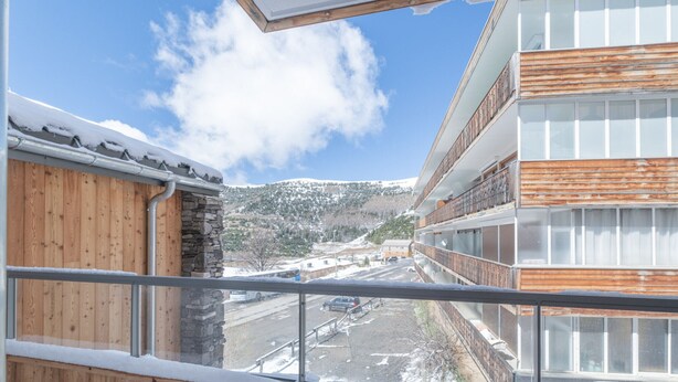 Un balcon donnant sur une montagne enneigée, un bâtiment en bois et une structure moderne dotée de balcons.