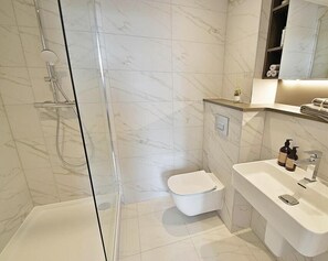 A modern bathroom with a glass-enclosed shower, a white toilet, and a sink with toiletries. - Top Floor 3-bed Penthouse in Manchester (Manchester)