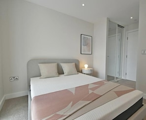 A bedroom with a bed, bedside table, and a door leading to another room. - Top Floor 3-bed Penthouse in Manchester (Manchester)