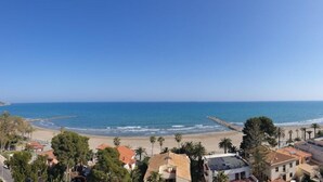 Une ville côtière dotée d’une plage, d’un ciel bleu azur et d’immeubles résidentiels aux toits recouverts de tuiles rouges.