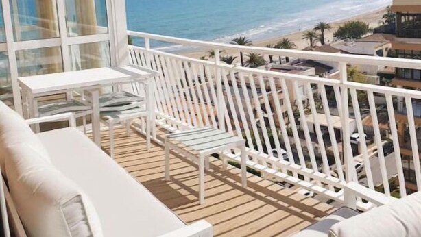 Un balcon doté de mobilier blanc, d’une table en verre et offrant une vue sur la plage et l’océan.
