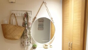 Une salle de bain avec une armoire en bois, un miroir rond, un panier suspendu et une petite étagère ornée d’objets décoratifs.
