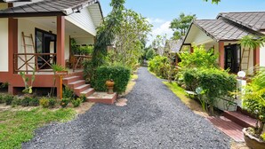 A pathway leading to a row of bungalow-style accommodations with a gravel path, surrounded by lush greenery and palm trees. - Tropical Heavens Garden Samui (Koh Samui)