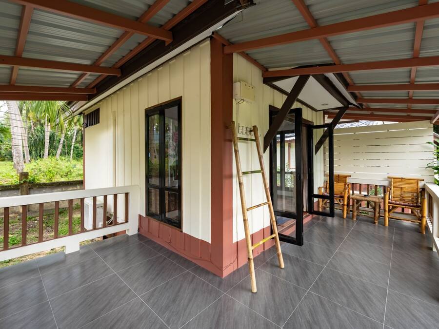 Een overdekt terras met betegelde vloer, een houten ladder en een zithoek met stoelen en een tafel.