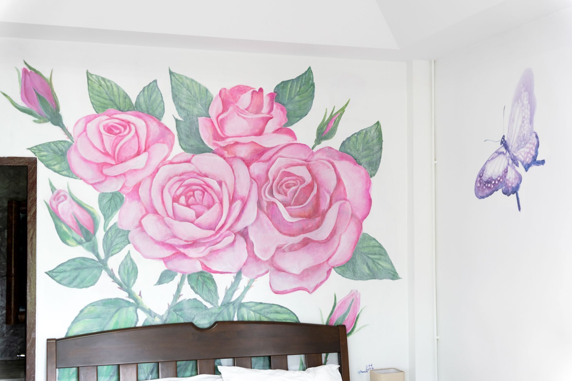 A bedroom with a bed, a wall mural of pink roses, and a butterfly.
