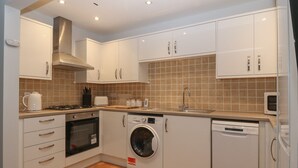 Une cuisine moderne avec des meubles blancs, une cuisinière, un four, un four à micro-ondes et un lave-linge.