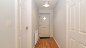 Un couloir étroit avec un plancher en bois, des murs blancs et une porte blanche au fond.