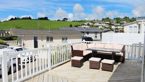 A deck with outdoor furniture, a white fence, and a view of a hillside with houses. - Charming 3-bed Chalet in Abersoch (Pwllheli)