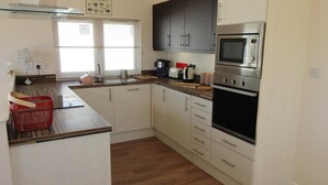 A compact kitchen with white cabinets, a microwave, a stove, and a sink. - Charming 3-bed Chalet in Abersoch (Pwllheli)