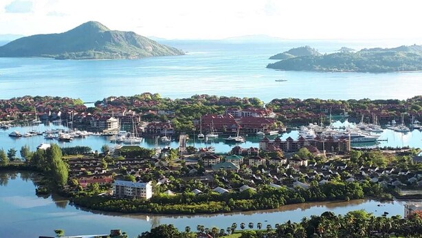 A coastal town with a marina, residential buildings, and a large mountain in the background. - Beau Soleil Stunning Sea View  (Mahé Island)