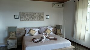 A bed with a wooden frame, white bedding, and two pillows with decorative patterns. - Beau Soleil Stunning Sea View  (Mahé Island)
