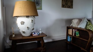 A living room with a white textured lamp on a wooden table, a bookshelf with books and decorative items, and a green and patterned wall art piece. - Beau Soleil Stunning Sea View  (Mahé Island)