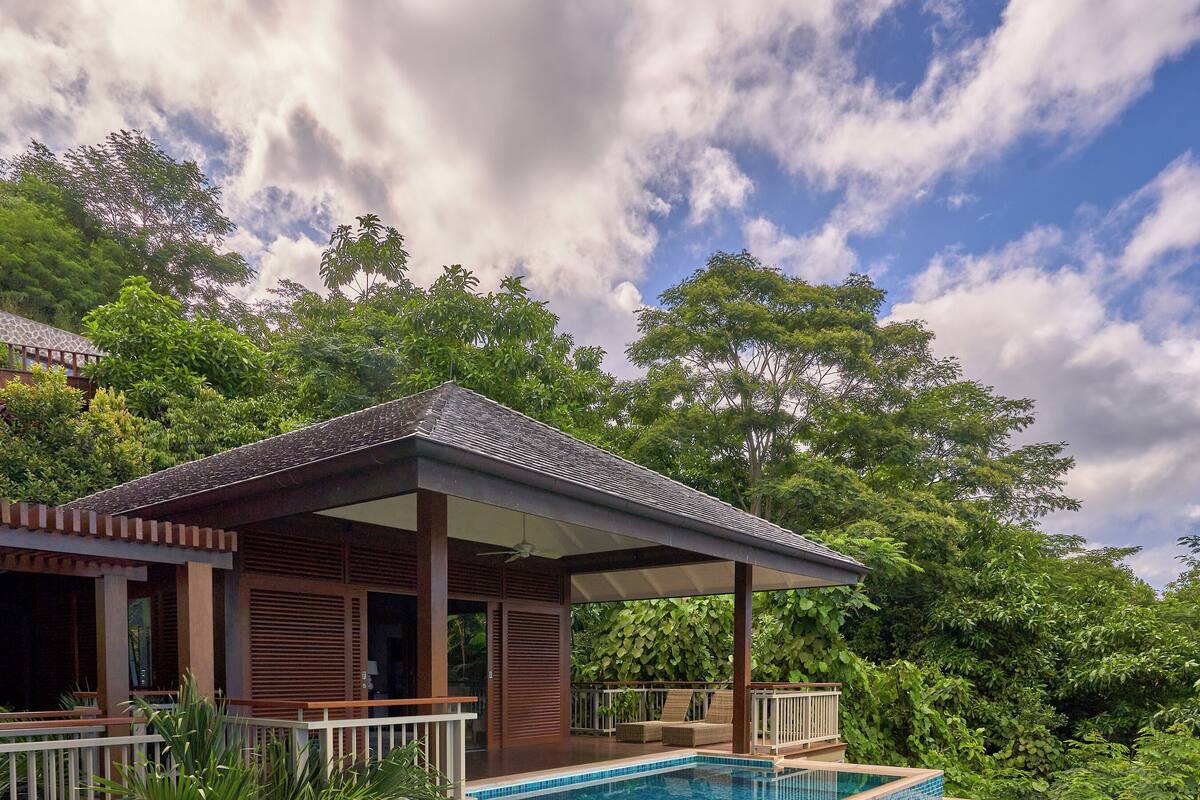 A poolside area with a stone structure, a covered seating area, and lush greenery.