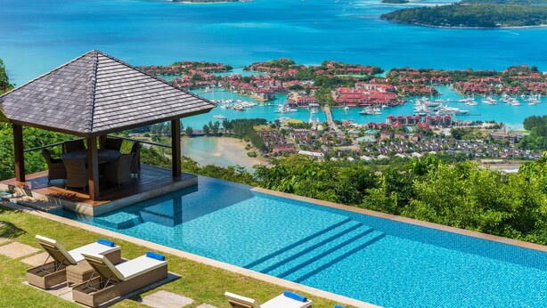 A pool area with lounge chairs, a covered seating area, and a view of a coastal town with boats and islands. - Villa Salazie (Mahé Island)