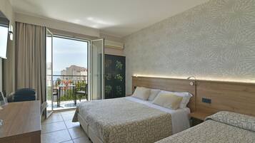 Ein Hotelzimmer mit Balkon, Schreibtisch, zwei Betten und einer Wand mit Muster.