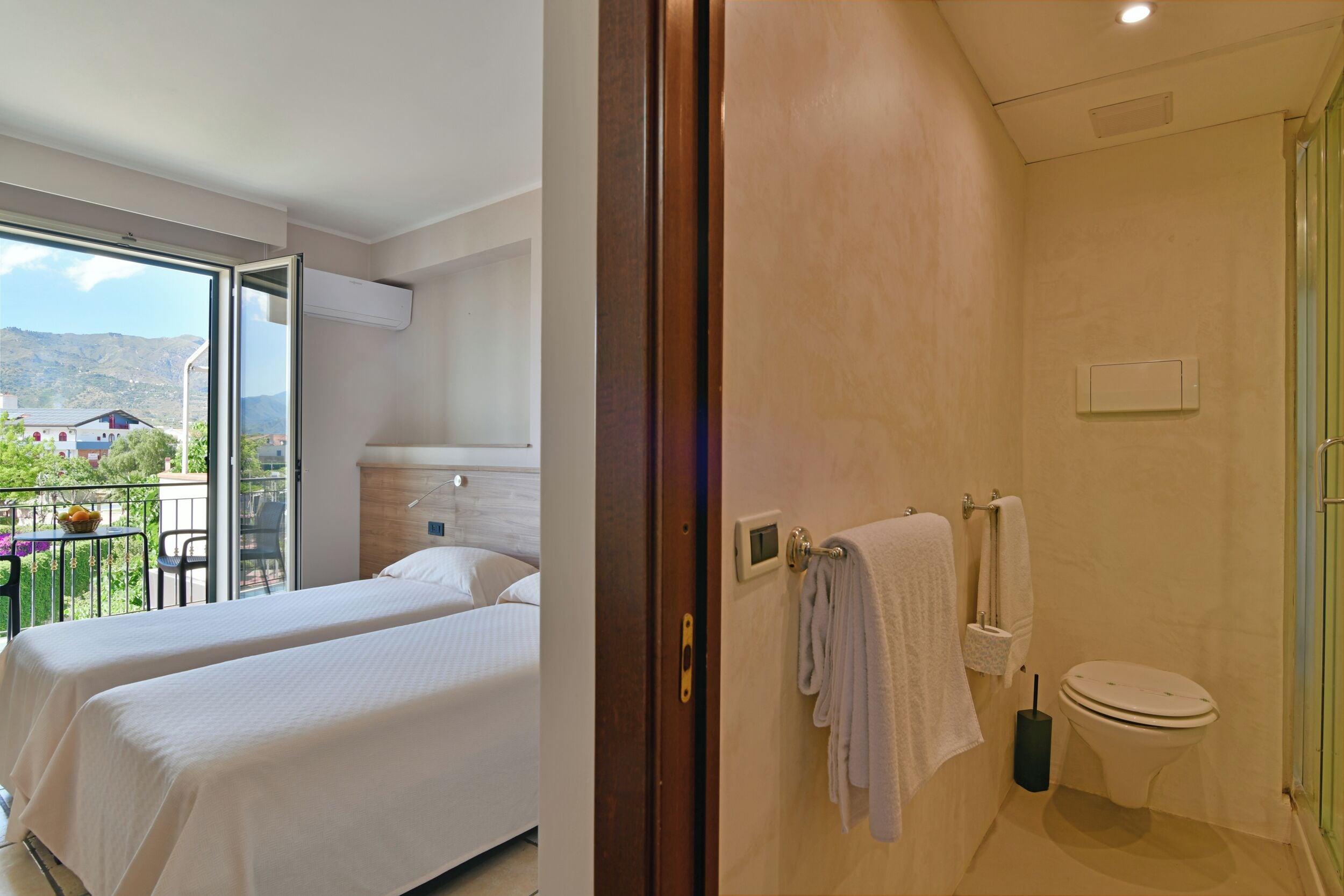 Habitación de hotel con dos camas, baño y balcón con vistas a las montañas.