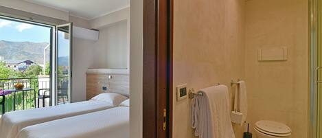 Habitación de hotel con dos camas, baño y balcón con vistas a las montañas.