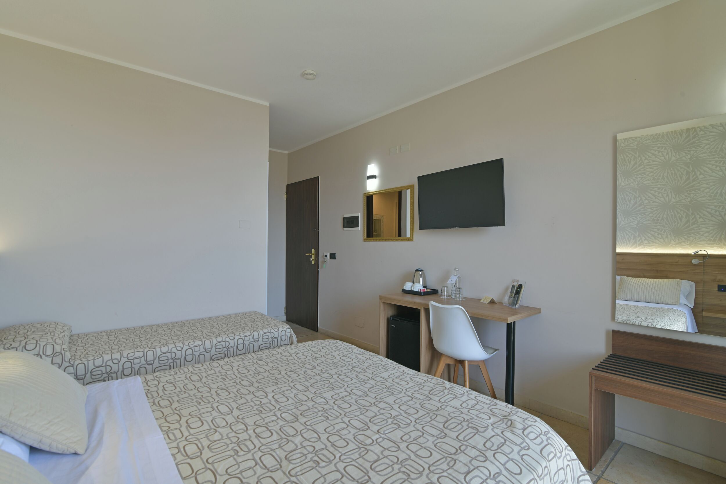 Ein Hotelzimmer mit zwei Betten, einem Schreibtisch mit Stuhl, einem Spiegel und einem kleinen Tisch.