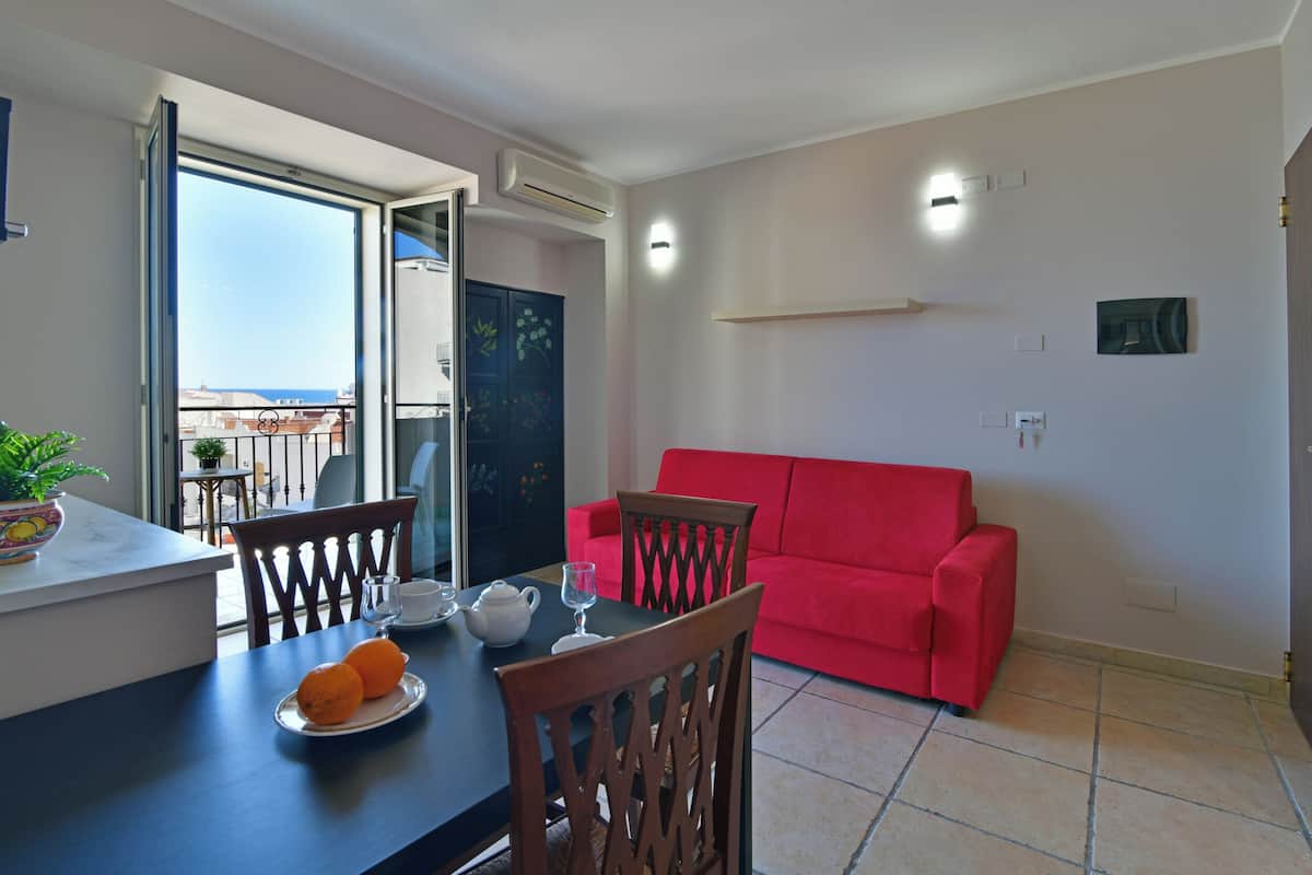 Un comedor con una mesa dispuesta para dos, un sofá rojo y un balcón con vistas.