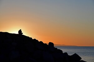 En siluett av en person som sitter på klippor i solnedgången.