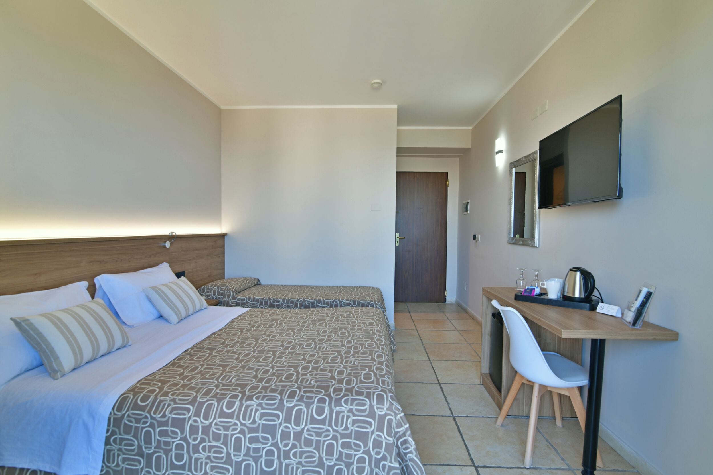 A hotel room with a bed, bedside table, chair, desk, and a television.