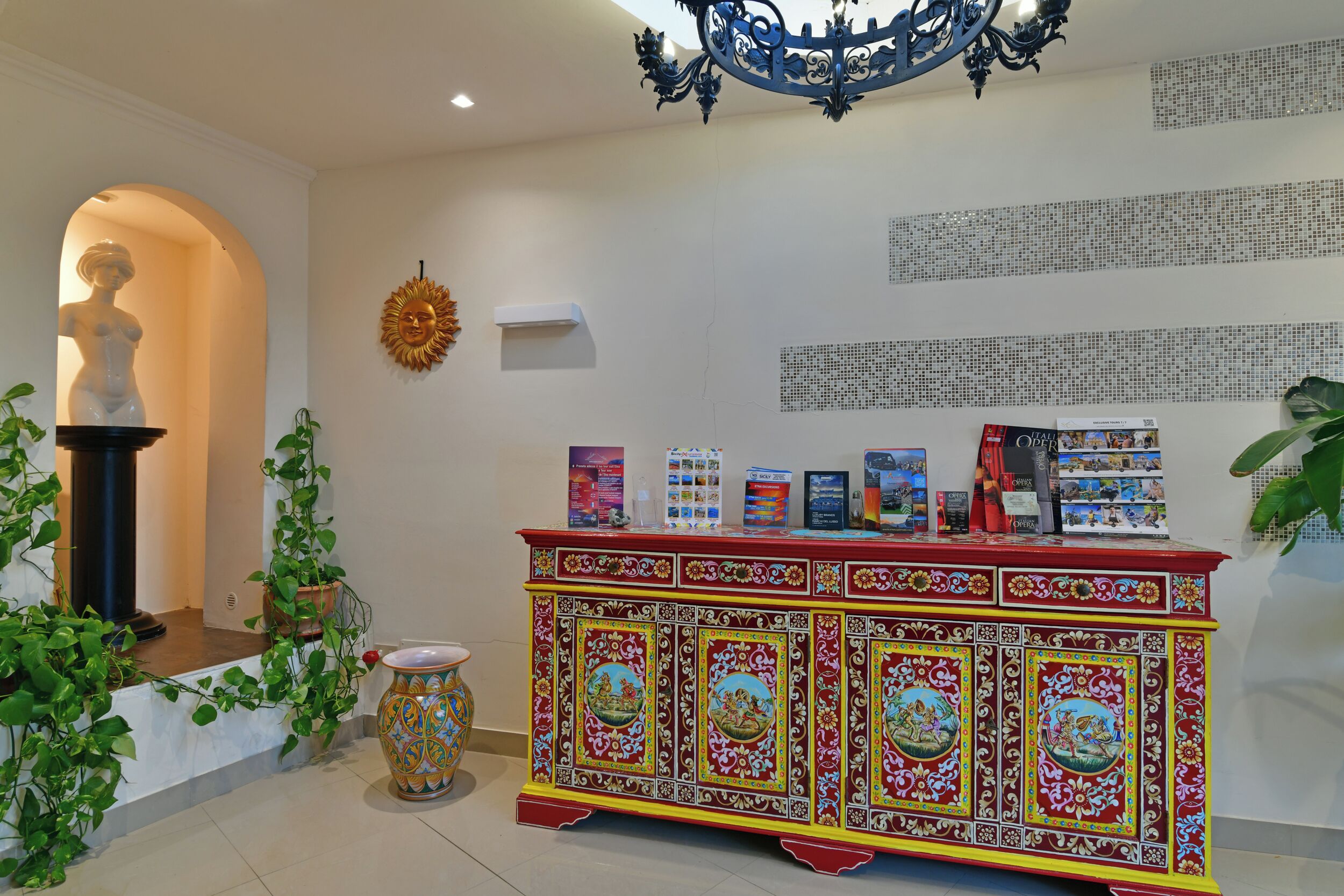 A reception area with a decorative red and yellow cabinet, a statue, and a wall with text.