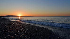 Ein Strand bei Sonnenuntergang mit Kiesstrand und ruhiger Wellenbewegung.
