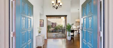 A hallway with blue doors, a chandelier, and a view into a dining area with a table and chairs.