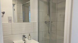 Un baño moderno con cabina de ducha de vidrio, un lavabo blanco con grifo y un espejo sobre el lavabo.