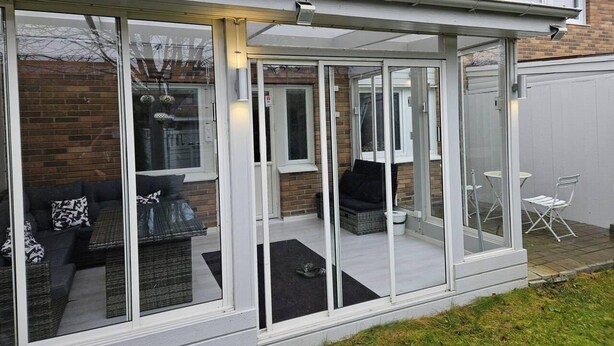 A modern house with a glass-enclosed patio area featuring outdoor furniture and a white exterior. - Unic House, Feeling Calmness in Malmo City (Malmö)