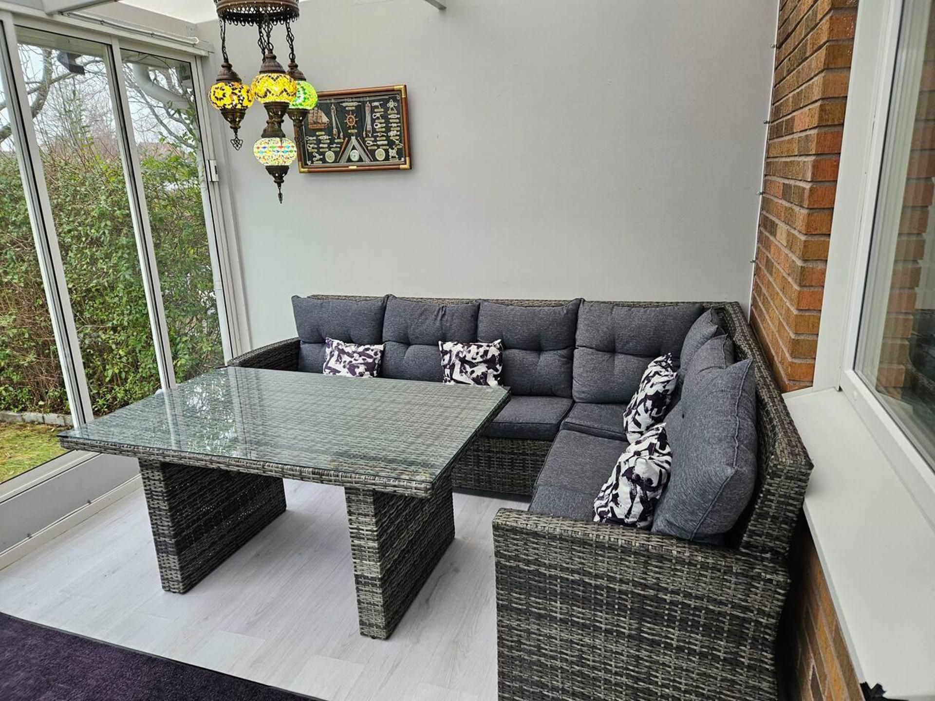 A corner room with a grey sectional sofa, a glass-top table, and wicker furniture.