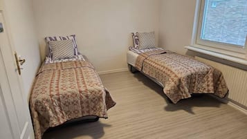 A small room with two single beds, a window with blinds, and a door with a brass handle.