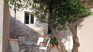 Un área de estar al aire libre con sillas y una mesa, rodeada de macetas con plantas y un árbol.