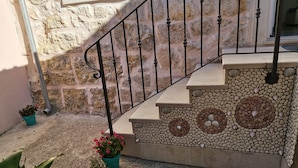 Una escalera de piedra con barandilla de metal que conduce a una puerta. Hay plantas en macetas en la base.