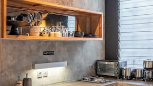 Eine moderne Küche mit Backofen, Toaster und Spüle. Darüber befindet sich ein Holzregal mit Küchenutensilien und einem dekorativen Gegenstand.
