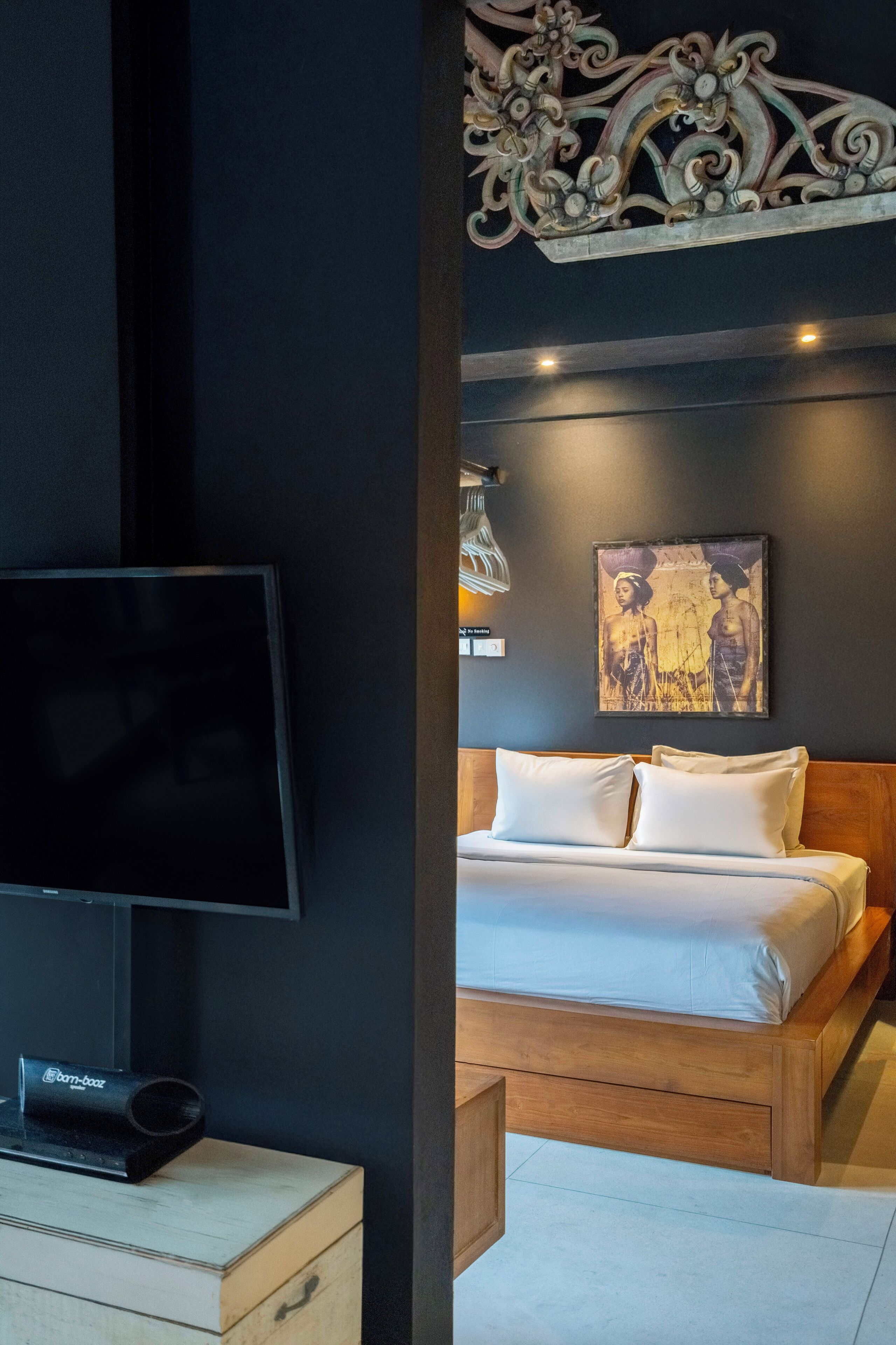 A modern bedroom with a flat-screen TV, a wooden bed frame, and a decorative wall piece.