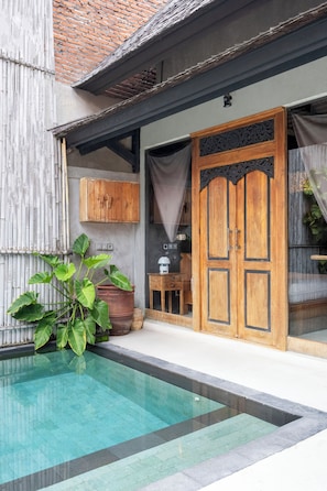 A pool area with a wooden door, a bamboo wall, and a potted plant. - Black House Villa by Betterplace (Canggu)