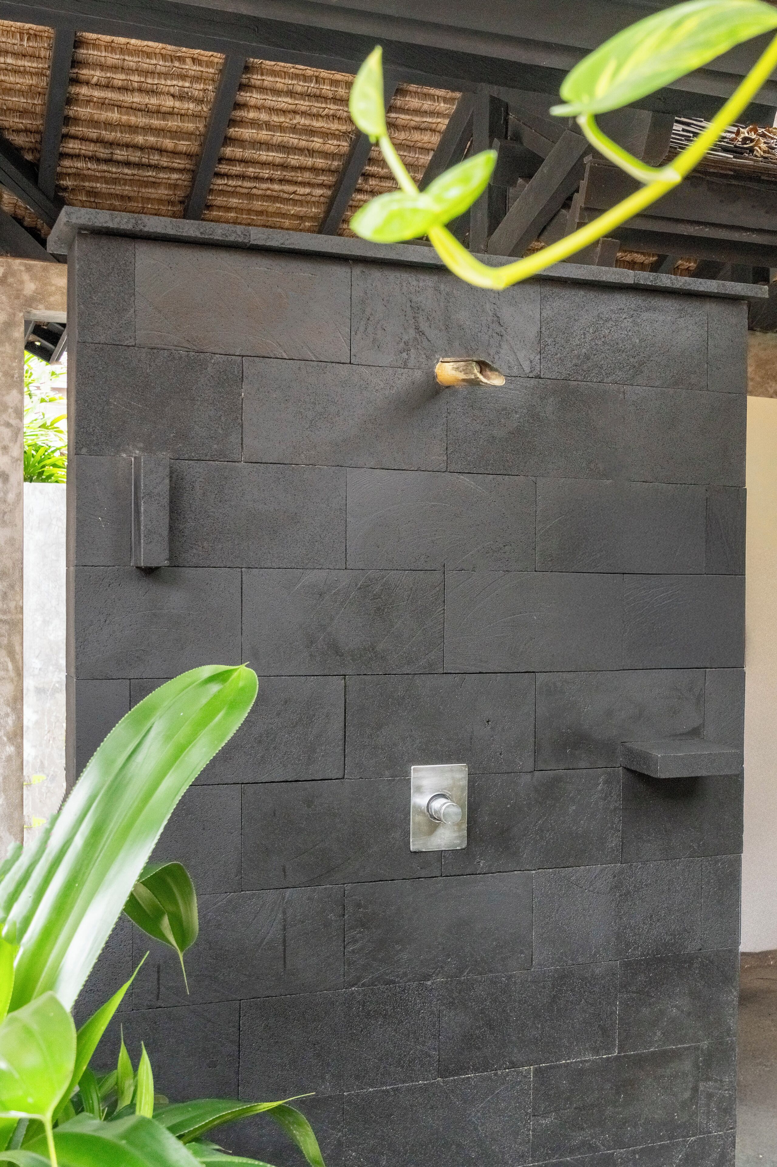 A black stone wall with a metal handle and a small metal plate, possibly a door or a panel.