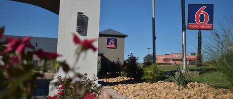 A motel sign with a number 6 and a 'motel + studio' label, surrounded by a landscaped area with rocks and plants.