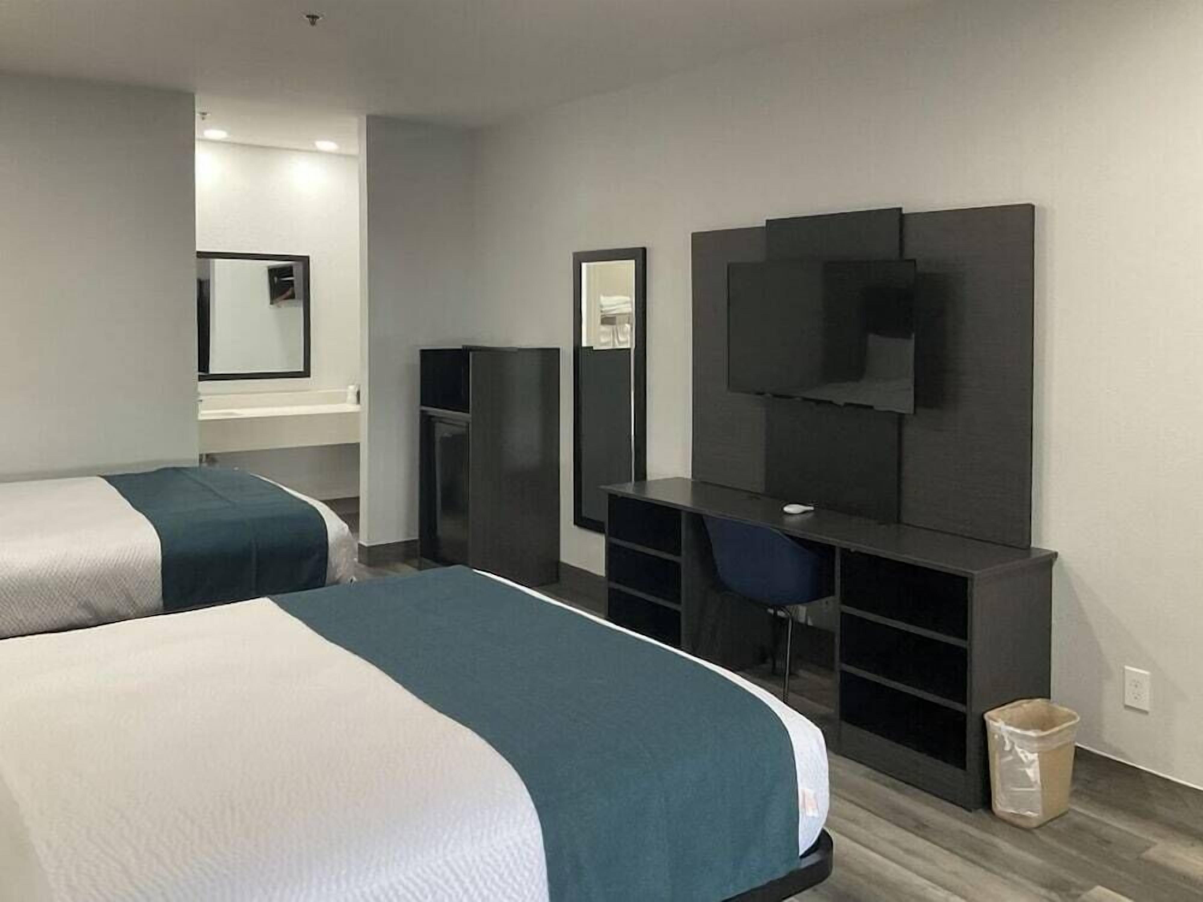 A hotel room with two beds, a desk, a TV, and a mirror.