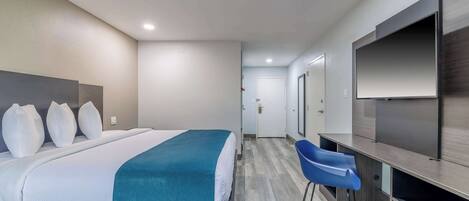A hotel room with a bed, a desk, a chair, a TV, and a door.
