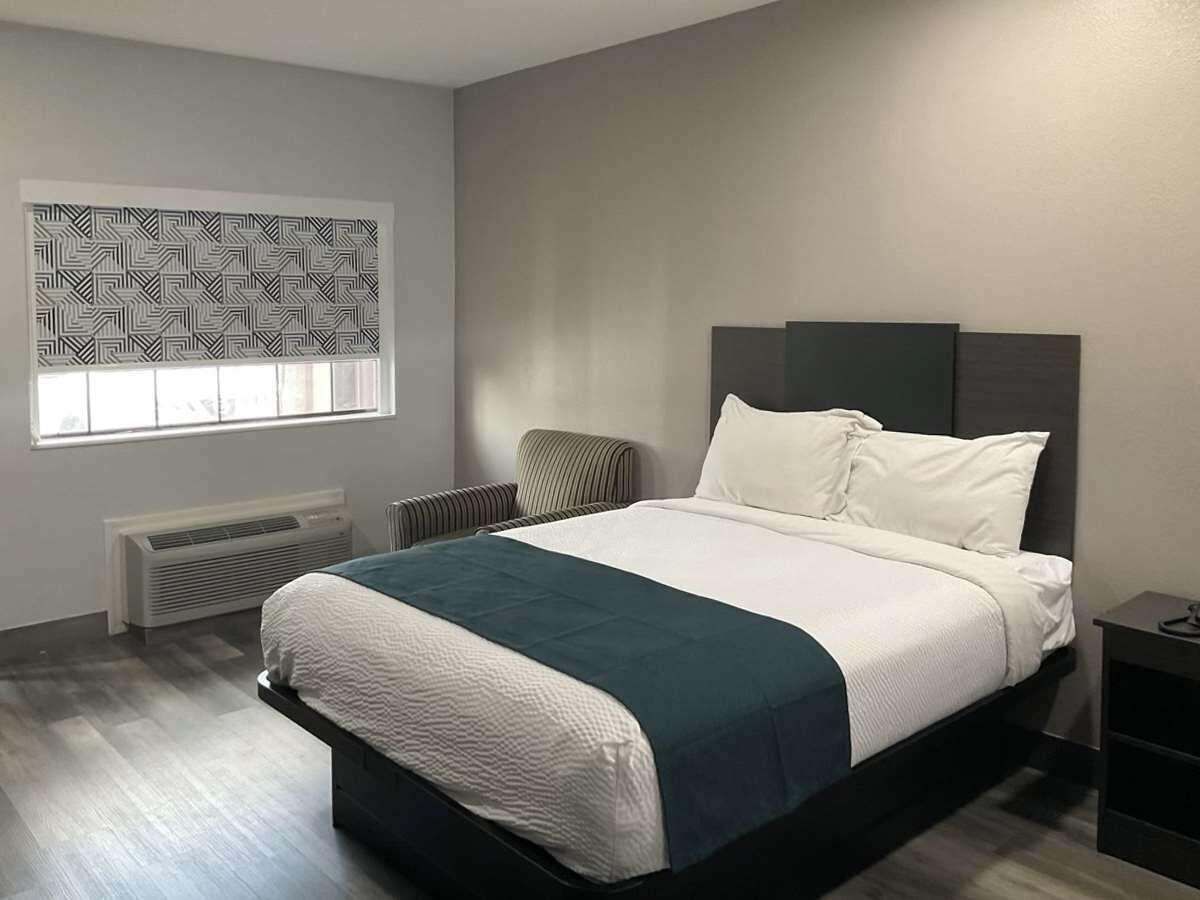 A modern bedroom with a large bed, a radiator, a window with blinds, and a chair.