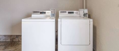 Two white front-loading washing machines in a laundry room with tiled flooring and a plain wall.