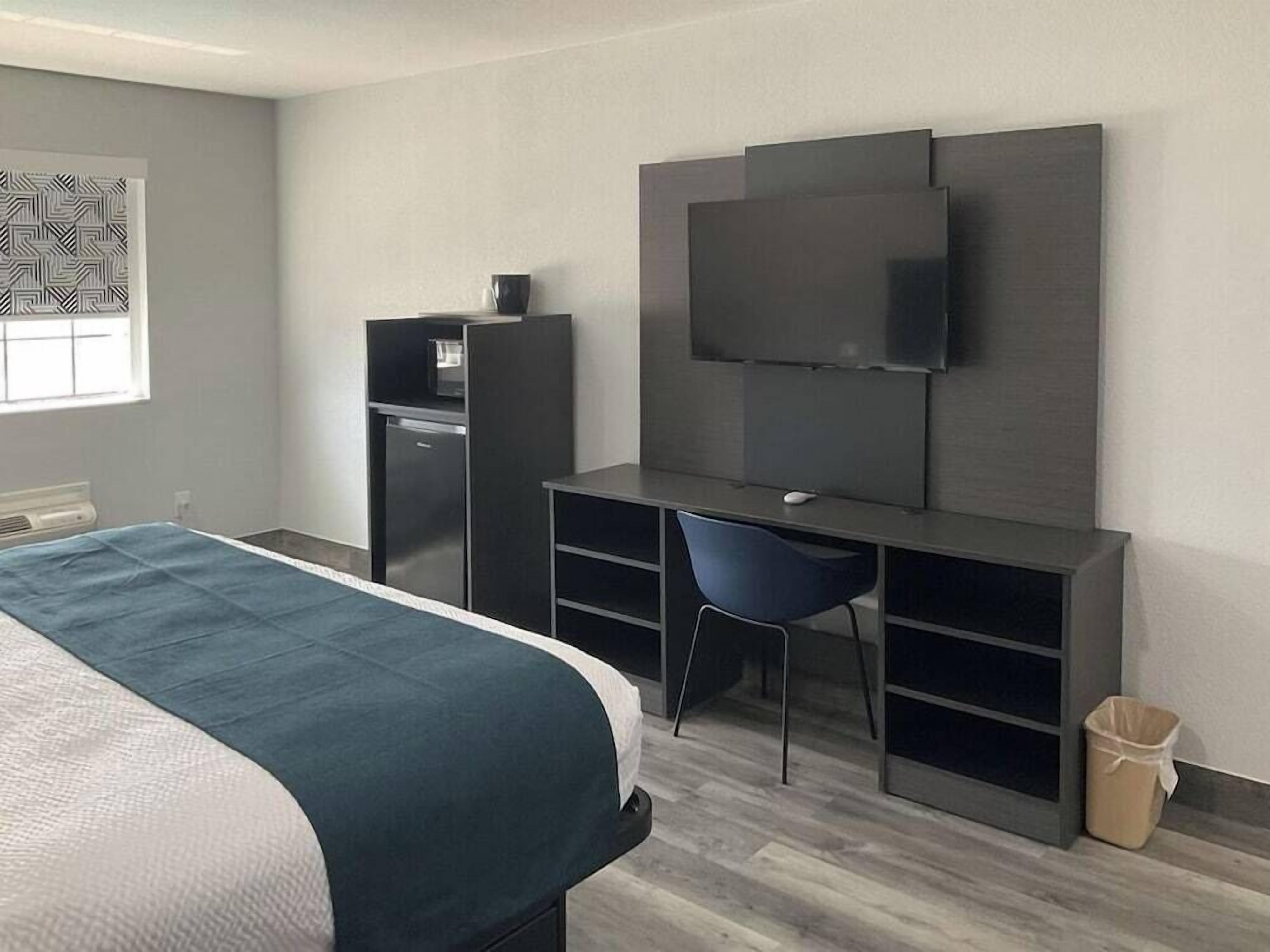Ein Hotelzimmer mit Bett, Schreibtisch mit Stuhl, Fernseher, einer kleinen Küchenzeile und einem Mülleimer.
