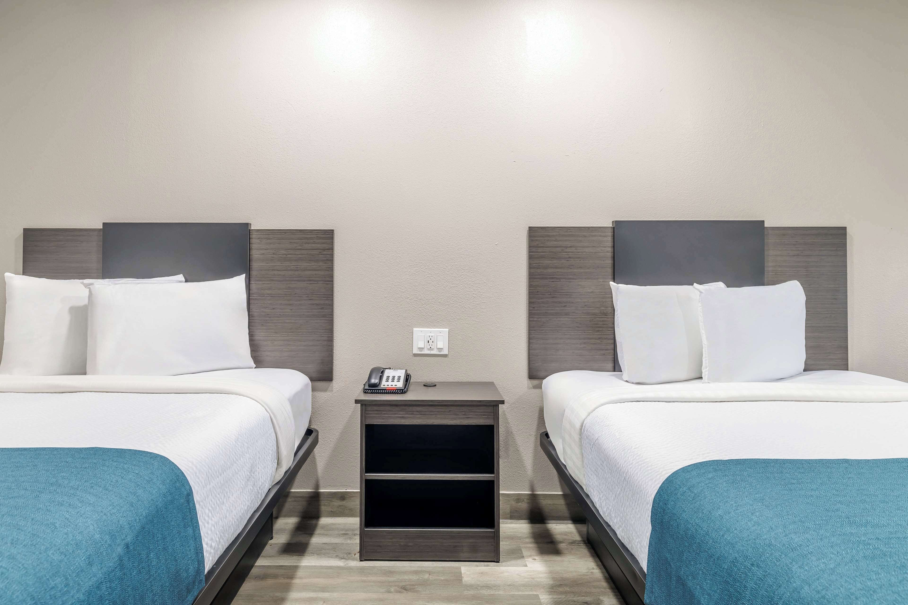 A hotel room with two beds, a nightstand with a phone, and a wall socket.