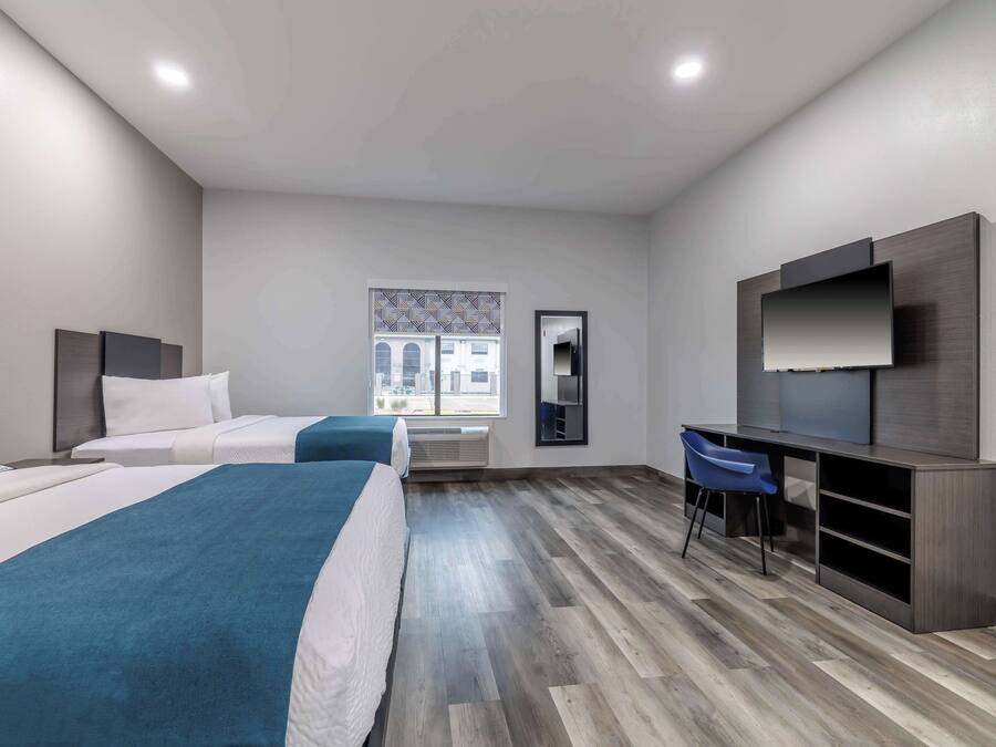 A hotel room with two beds, a desk with a chair, a TV, and a window with a view of buildings.