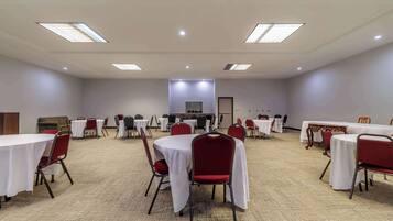 Un salón de conferencias con varias mesas y sillas, piso alfombrado e iluminación en el techo.