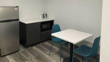 A compact kitchen with a refrigerator, a microwave, and a small countertop. There are two blue chairs and a white table.