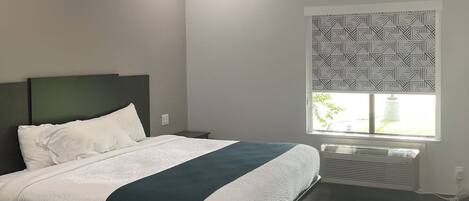 A modern bedroom with a bed, a nightstand, a window with a geometric pattern, and a radiator.